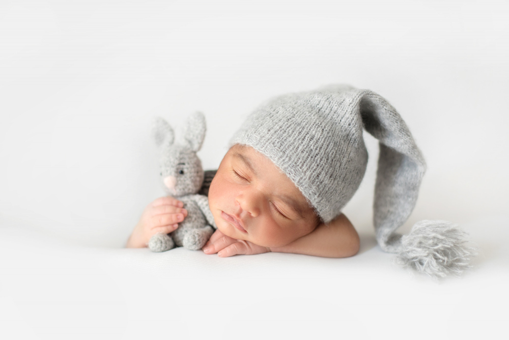 cute infant sleeping with grey crocheted hat with toy rabbit