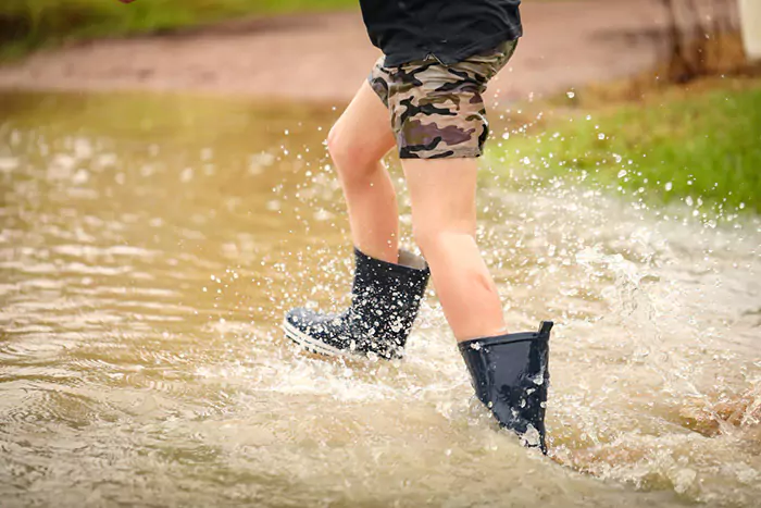 boy walking through flooded creek wearing gumboots n