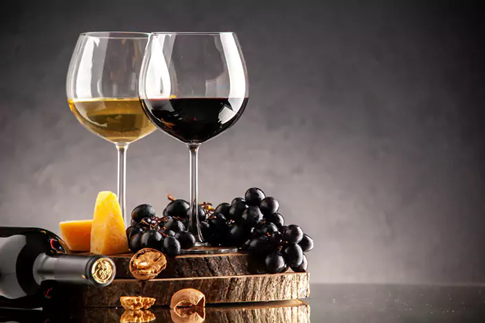 front view wine glasses fresh grapes walnuts yellow cheese wood board overturned bottle dark background 6489a9549cc68