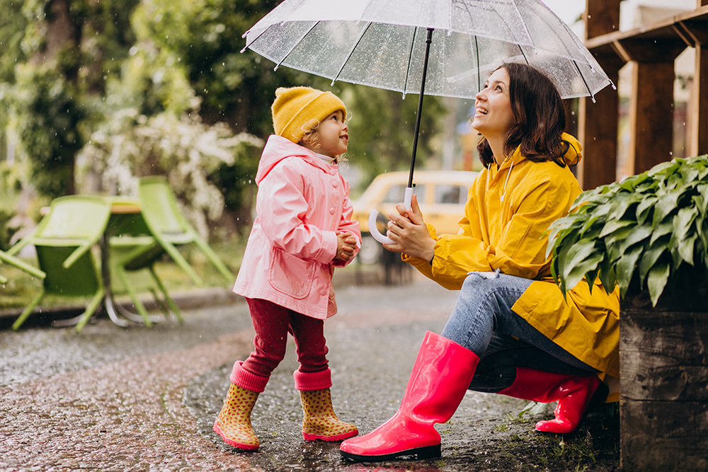 mother with daughter walking in park in the rain wearing rubber boots