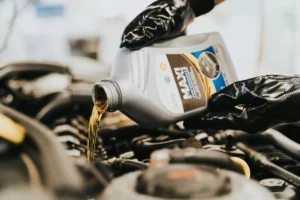 Motorno ulje se sipa iz boce u motor dok ruka u crnim rukavicama drži bocu