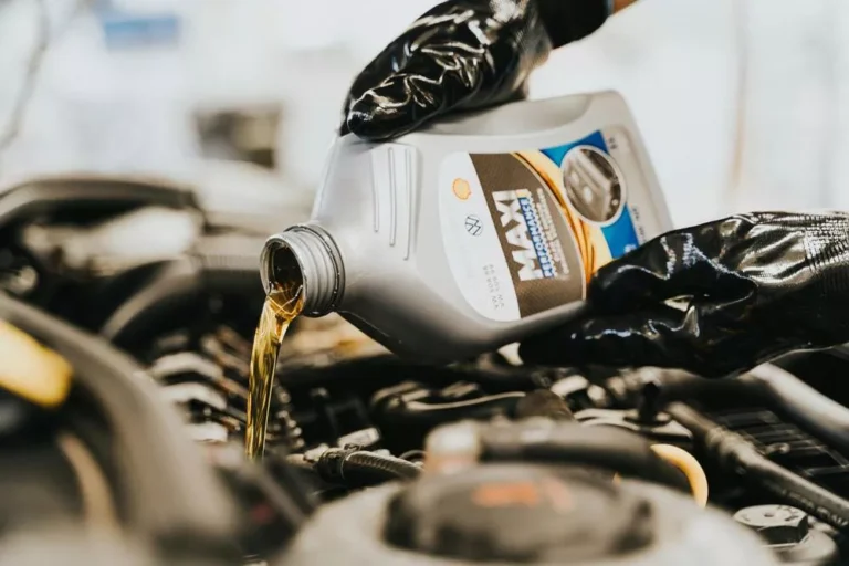Motorno ulje se sipa iz boce u motor dok ruka u crnim rukavicama drži bocu